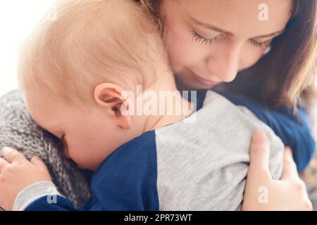 Mama wird dich immer lieben, mein kleiner Engel. Eine kurze Aufnahme einer Mutter, die ihren verschlichen Jungen zu Hause hält. Stockfoto