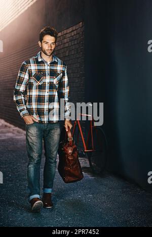 Stilvolles Design für das Leben in der Stadt. Aufnahme eines hübschen jungen Mannes, der eine Tasche trägt und eine Straße entlang geht. Stockfoto