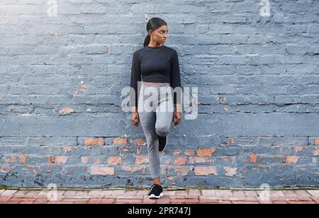 Gekleidet für Fitness-Erfolg. Aufnahme einer jungen Frau, die sich im Freien an einer grauen Wand lehnt. Stockfoto