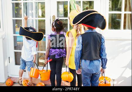 Auf der Suche nach Süßigkeiten. Aufnahme einer Gruppe von nicht erkennbaren kleinen Kindern, die sich mit einem Trick-or-Treating abfinden. Stockfoto