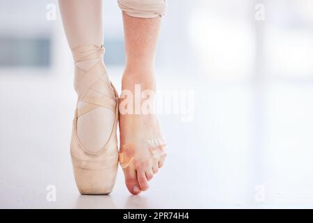 Ich sollte meine Füße auf jeden Fall öfter verkleben. Eine kurze Aufnahme einer jungen Ballerina, die einen spitzenschuh auf einem Fuß trägt und Barfuß mit einem Band. Stockfoto