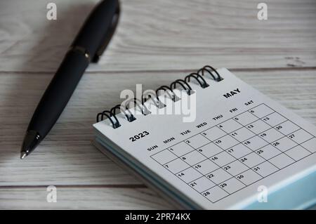 Weißer Schreibtischkalender Mai 2023 mit schwarzem Stift auf Holztisch. Stockfoto