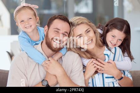 Fröhliche, vierköpfige, weiße Familie, die zu Hause auf einem Sofa gelächelt hat. Sorglos liebende Eltern, die sich mit zwei süßen kleinen Töchtern verbinden. Süße junge, verspielte Mädchen, die mom und Dad umarmen Stockfoto