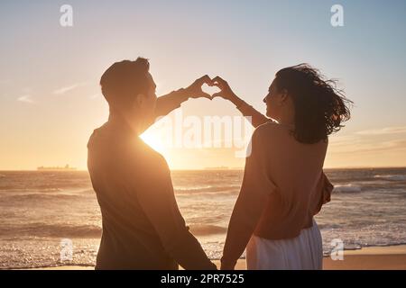 Biracial Paar hält ihre Hände in einer Herzform am Strand zusammen. Stockfoto