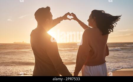 Ein birassisches Paar, das am Strand die Hände in Herzform zusammenhält. Ein birassisches Paar, das am Strand die Hände in Herzform zusammenhält. Stockfoto