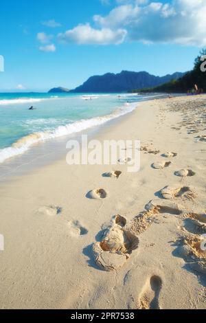 Ein leerer Strand, entspannende Sommerlandschaft für einen friedlichen Urlaub mit klarem blauen Himmel und Fußabdrücken in der Sandtapete. Wellen, die sich an die Sandküste des tropischen und exotischen Resorts schwingen Stockfoto