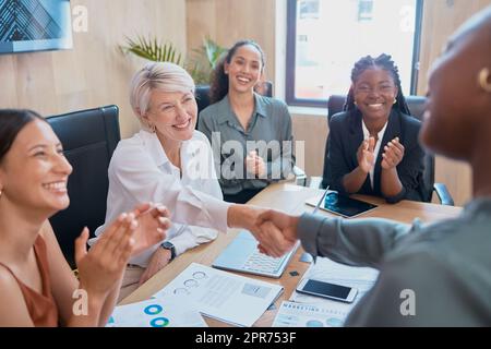 Handschlag zwischen Geschäftsfrauen. Zwei verschiedene Kollegen schütteln sich während einer Besprechung im Sitzungssaal die Hand. Sie zu ihrer guten Arbeit beglückwünschen, während Kollegen klatschen und ihre Leistung anerkennen Stockfoto