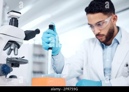 Ein gemischter Wissenschaftler trägt eine Schutzbrille und einen Labormantel, während er medizinische Forschungsexperimente mit Pipetten und Reagenzgläsern in einem Labor durchführt. Aufzeichnung seiner Ergebnisse für zukünftige Untersuchungen Stockfoto