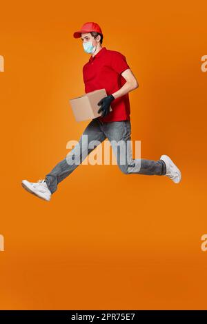 Delivery Mann in Gesichtsmaske hält Pappkarton und springen Stockfoto