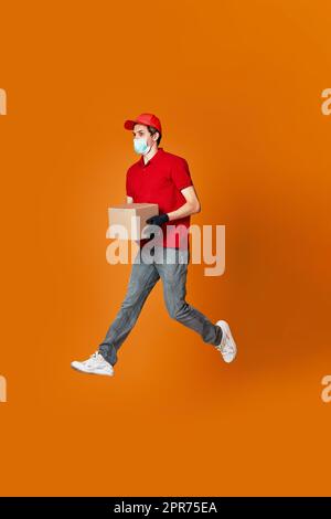 Delivery Mann in Gesichtsmaske hält Pappkarton und springen Stockfoto