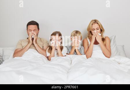 Durch dick und dünn. Aufnahme einer jungen Familie, die zusammen krank im Bett aussieht. Stockfoto