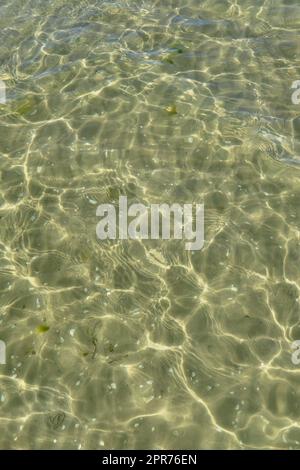 Blick über das Sonnenlicht, das vom Wasser am Strand reflektiert wird, mit Kopierbereich. Flache Wellen und ruhige Wellen an der Küste an sonnigen Tagen draußen. Klare, flüssig brechende Sonnenstrahlen vor Sommerhintergrund Stockfoto