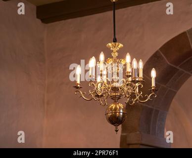 Altmodischer Messingkronleuchter mit Kerzenlampen, die vom Dach oder von der Decke hängen, in einem historischen Gebäude und einem alten Raum. Glänzende dekorative, mittelalterliche, antike und antike Leuchten in einem Herrenhaus Stockfoto