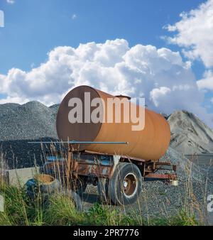 Ein alter Wassertanker, der auf der Baustelle verrottet. Verrosteter Wasserbehälter in der Nähe eines Haufens aus Beton und Zement. Verlassener alter rostiger Wassertank in der Bauindustrie in der Nähe eines Sand- und Kies-Haufens Stockfoto