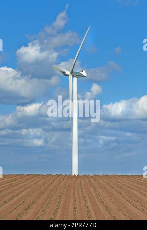 Windturbinen auf einem Bauernhof mit neu gepflanzten Pflanzen. Bewölkter Tag auf landwirtschaftlichen Flächen, wo Windenergie die wichtigste Ressource ist. Erzeugung von nachhaltigem Strom und frischen Erzeugnissen Stockfoto