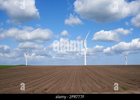 Windturbinen und Umweltinfrastruktur isoliert gegen blauen Himmel mit Kopierraum auf einem leeren Energiefarm. Propeller, die nachhaltige Energie in elektrische Energie in abgelegenen und ländlichen Gebieten umwandeln Stockfoto