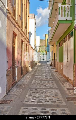 Leere Kopfsteinpflasterstraße in einer ländlichen europäischen Touristenstadt. Eine ruhige, enge Gasse mit bunten Apartmentgebäuden oder Häusern. Versteckte Seitenstraße mit traditioneller Architektur in Santa Cruz de La Palma Stockfoto