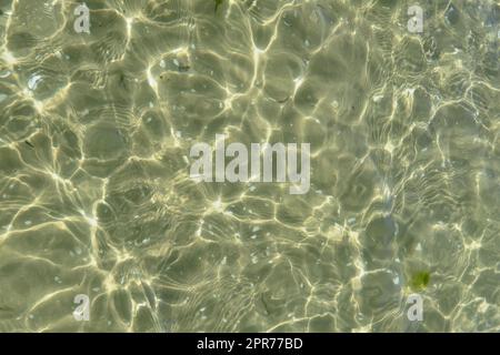 Blick über das Sonnenlicht, das auf dem Wasser am Strand reflektiert. Nahaufnahme von flachen Wellen und ruhigen Wellen an der Küste an sonnigen Tagen draußen. Klare, flüssig brechende Sonnenstrahlen im Sommer für den Hintergrund des Kopierraums Stockfoto