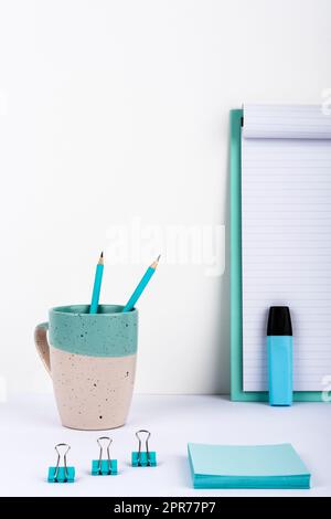 Becher Mit Zwei Bleistiften Auf Dem Schreibtisch Mit Klemmbrett Mit Wichtiger Nachricht, Büroklammern, Marker Und Notizen. Tasse Mit Stiften Auf Dem Tisch Mit Memos Mit Grausamkeiten Präsentiert. Stockfoto