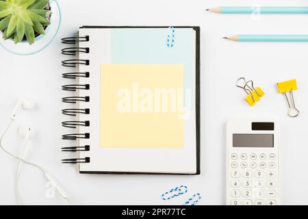 Notizbuch Mit Wichtiger Nachricht Am Schreibtisch Mit Stiften, Taschenrechner, Kopfhörern, Blumen Und Büroklammern. Notizblock Mit Informationen Auf Dem Tisch Mit Bleistiften Und Farbigen Clips. Stockfoto