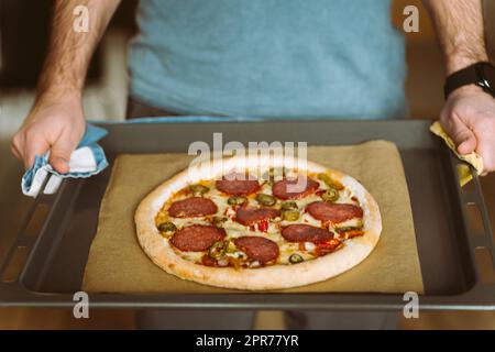 Ein Mann hält ein Backblech mit Pizza. Backpapier mit Backpapier bedeckt Stockfoto