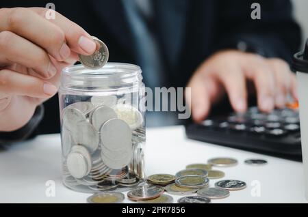 Pensionsplanung oder Anlagebuchhaltung Geschäftskonzept zur Finanzierung der Versicherungssteuer. Ein Geschäftsmann, der Geld in einer Dose und einem Taschenrechner am Schreibtisch hält. Stockfoto