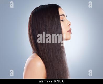 Profilansicht eines wunderschönen braunhaarigen Mädchens mit glattem und glänzendem Haar vor grauem Hintergrund. Junge brünette Frau mit schönen langen, glatten Haaren Stockfoto