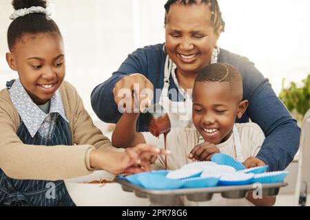 Also machen Sie extra, um nach Hause zu nehmen. Aufnahme einer Großmutter, die mit ihren beiden Enkelkindern zu Hause backt. Stockfoto