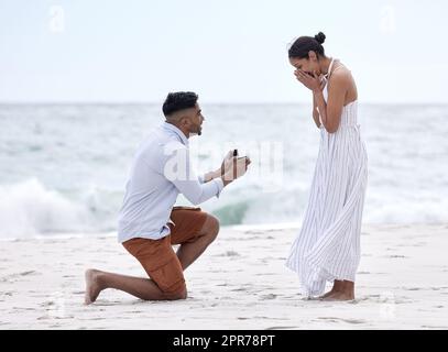 Wirst du mich heiraten? Ganzkörperaufnahme eines hübschen jungen Mannes, der seiner Freundin am Strand vorschlägt. Stockfoto