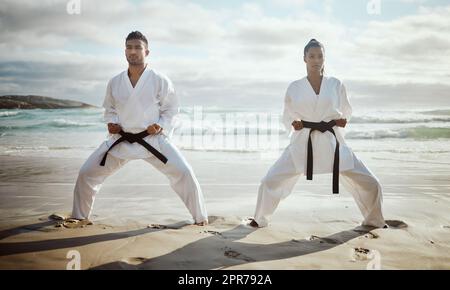 Bereit für einen Kampf. Ganzkörperaufnahme von zwei jungen Kampfkünstlern, die am Strand Karate üben. Stockfoto
