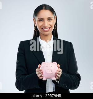 .. Ein junges Weibchen, das ein Sparschwein vor grauem Hintergrund hält. Stockfoto