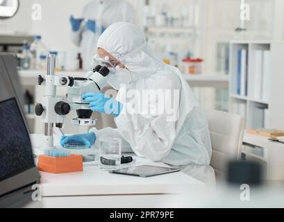 Es ist klar, jetzt zu sehen. Ein Wissenschaftler trägt einen Strahlenanzug, während er ein Mikroskop in einem Labor benutzt. Stockfoto