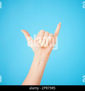 Hey, was ist da? Studioaufnahme einer nicht erkennbaren Frau mit einem shaka-Handzeichen vor blauem Hintergrund. Stockfoto