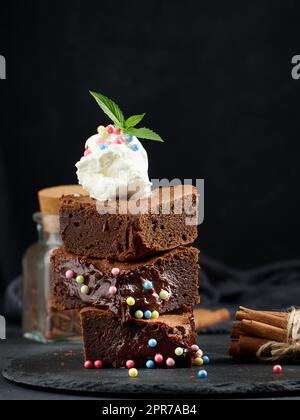 Gebackene Brownie-Schokoladenstückchen auf einem schwarzen Tisch, auf einer Kugel Eis Stockfoto