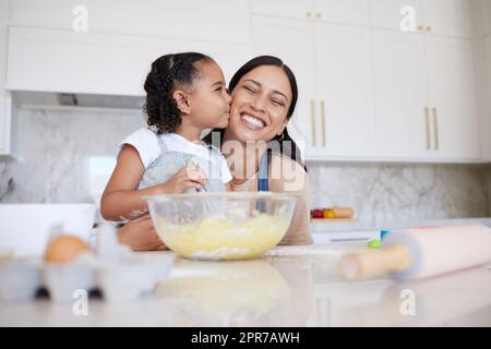 Mutter und Tochter backen zusammen in einer Hausküche. Ein fürsorgliches kleines, bezauberndes Mädchen, das ihre alleinerziehende Mutter auf die Wange küsst. Glückliche Frau und liebevolles Kind, das sich innen anfreundet und kochen lernt Stockfoto