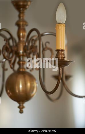 Die Vervollständigung eines alten Messingleuchters, der während eines Verdunkelungsvorgangs als Dekoration in einem Foyer, einer Eingangshalle oder einem Speisesaal hängt. Einrichtung in goldener Kerzenform mit Innenausstattung im königlichen viktorianischen Stil Stockfoto