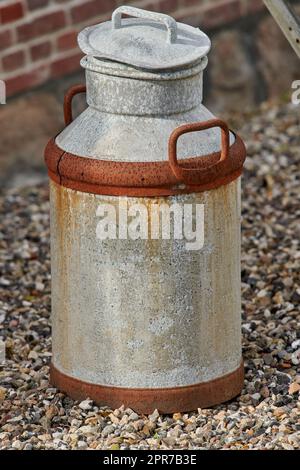 Eine alte, verrostete Metallmilchdose auf dem Boden von oben. Ein antiker Milchkanister draußen auf einem mit Kieseln überdachten Gang. Eine rostige und gebrauchte Metallkanne tagsüber mit Kopierraum Stockfoto