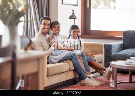 Sie sind mein Stolz und meine Freude. Porträt eines hübschen jungen Mannes und seiner beiden Töchter, die zu Hause auf dem Sofa sitzen. Stockfoto