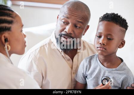 Eine afroamerikanische Kinderärztin untersucht einen kranken Jungen mit Stethoskop während des Besuchs mit dem Vater. Arzt kontrolliert Herz und Lunge bei der Untersuchung im Krankenhaus. Kranker oder trauriger Junge, der medizinisch versorgt wird Stockfoto