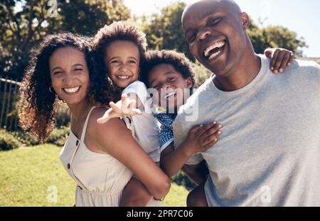 Fröhliche junge afroamerikanische Eltern, die mit ihren kleinen Söhnen im Garten spielen. Aufgeregte Mutter und Vater, die ihre Söhne auf Huckepackfahrten tragen. Lächelndes Paar, das einen Tag im Park genießt Stockfoto