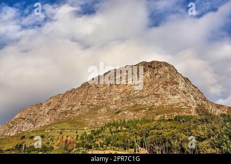 Ein Bild von unten vom Tafelberg. Ein wunderschöner Blick auf die Natur auf einen hohen Berg, der wie ein Löwenkopf mit Wald geformt ist, und einen bewölkten Himmel im Hintergrund. Kopieren Sie Platz mit malerischer Landschaftsansicht Stockfoto