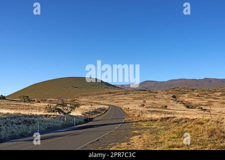 Straße durch die Landschaft am Mauna Loa - der größte Vulkan, Big Island. Ein wunderschöner Blick am Morgen von der Straßenseite des Mauna Loa, der größten Vulkaninsel. Stockfoto