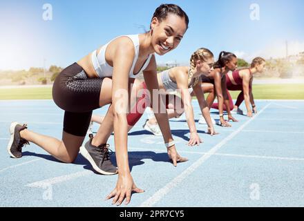 Porträt einer Sportlerin, die motiviert ist und bereit ist, bei der olympischen leichtathletik anzutreten. Vielfältige Gruppe von Wettkampffrauen mit Händen an der Startlinie, bereit für das Rennen und entschlossen, zu gewinnen Stockfoto