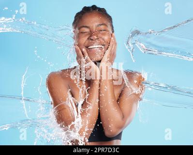 Ihre Wärme wird dich anziehen. Aufnahme einer schönen jungen Frau, die vor blauem Hintergrund mit Wasser bespritzt wurde. Stockfoto