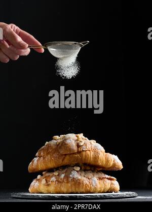 Gebackene Croissants auf einem Brett und bestreut mit Puderzucker, schwarzem Tisch. Appetitliches Gebäck zum Frühstück Stockfoto