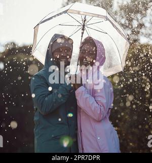 Wir lieben den Regen. Ein liebevolles Paar, das unter einem Regenschirm steht, während draußen im Regen. Stockfoto