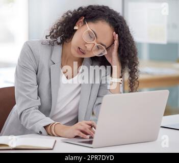 Wie werde ich das alles machen? Eine attraktive junge Geschäftsfrau, die allein in ihrem Büro sitzt und sich gestresst fühlt, während sie ihren Laptop benutzt. Stockfoto