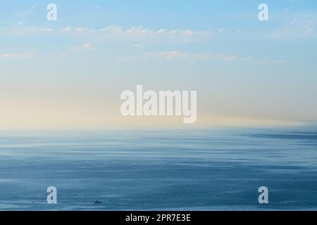 Ein leerer Ozean mit blauem Himmel und Kopierraum. Ein breiter offener Meereslandschaft Hintergrund eines Strands mit ruhigem Wasser. Malerische Meeresoberfläche mit beruhigenden Wellen und der aufgehenden Morgensonne am Horizont Stockfoto