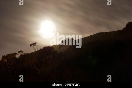 Silhouette einer sonderbaren Landschaft bei Nacht mit einem strahlenden Vollmond in Südafrika. Geheimnisvolle dunkle Naturszene an einem abgelegenen Ort am Abend. Gruseliger schwarz-weißer Hügel mit Schatten Stockfoto