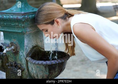 Porträt einer jungen Frau, die sich während der Hitzewelle im Sommer mit Trinkwasser aus einem Brunnen versorgt Stockfoto